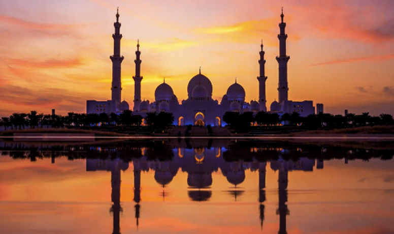 Silhouette of a mosque at sunset, reflecting in water, symbolizing innovation and cultural richness in the UAE.